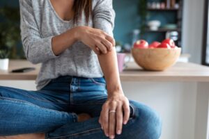 Young woman scratching her arm while sitting on the stool in the home kitchen.